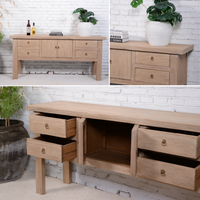 Wooden console with multiple drawers and open cabinet against a white brick wall.