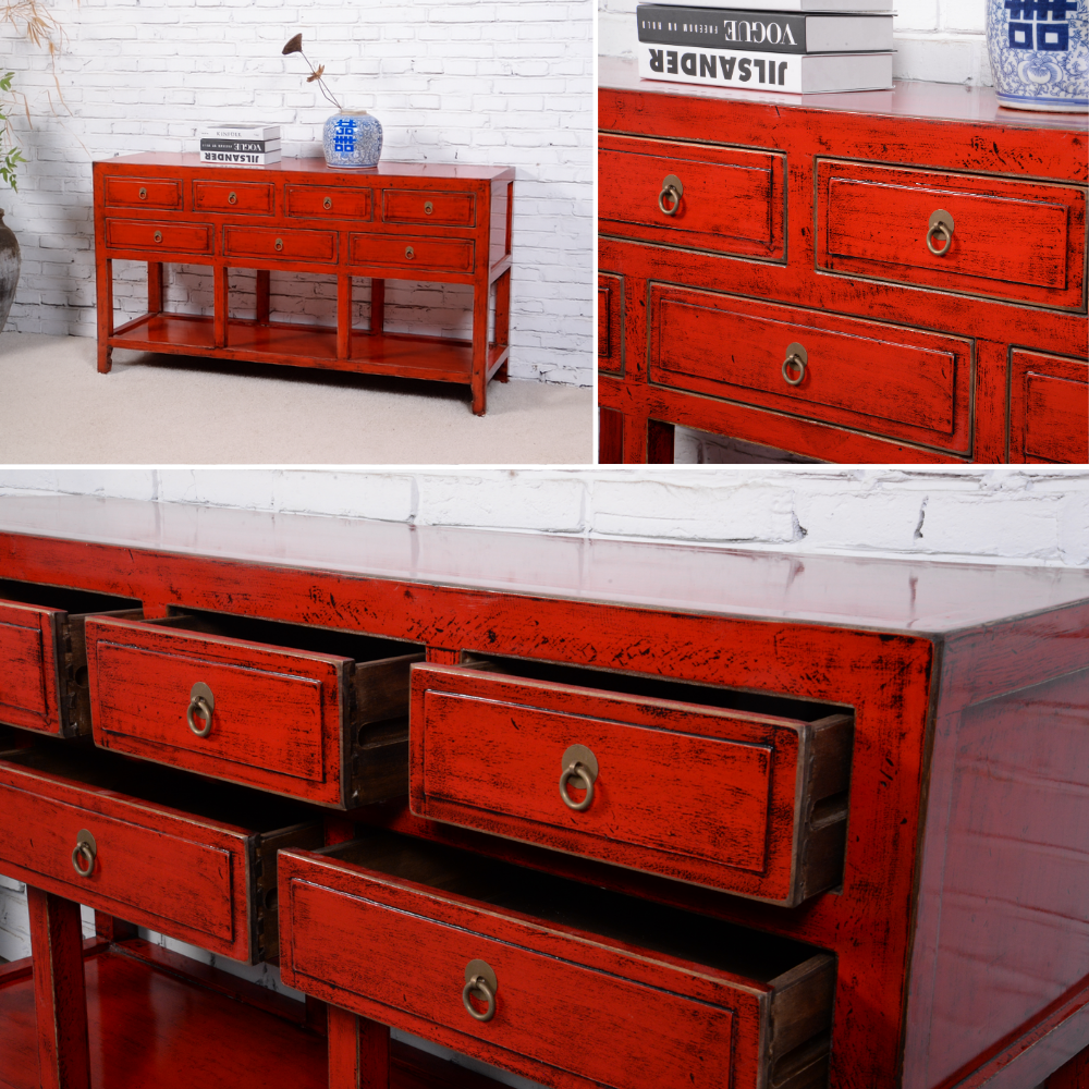 Red wooden console table with multiple drawers against a white brick wall.