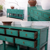 Teal wooden console table with drawers against a white brick wall.