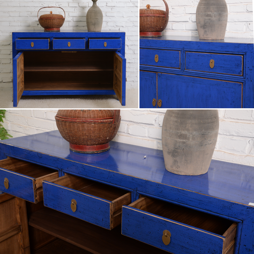 Blue wooden sideboard with drawers and decorative items against a white brick wall.