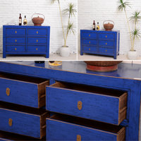 Blue wooden dresser with multiple drawers against a white brick wall.