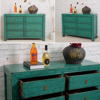 Teal dresser with decorative items against a white brick wall.