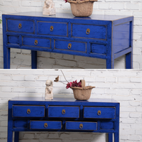 Blue wooden console table with drawers against a white brick wall.