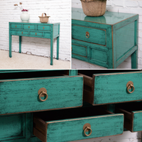 Teal wooden dresser with brass handles against a white brick wall.